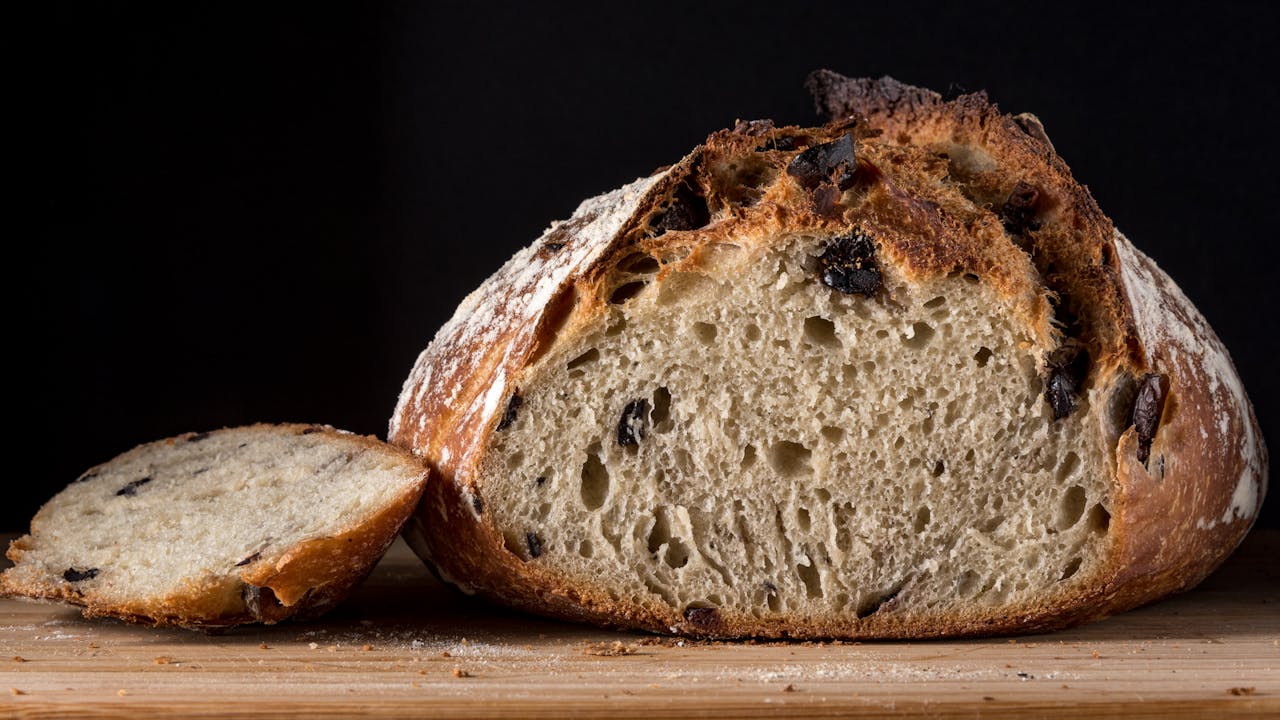 about-us-01 Delicious artisan olive bread loaf with one slice on wooden board, perfect for healthy eating.